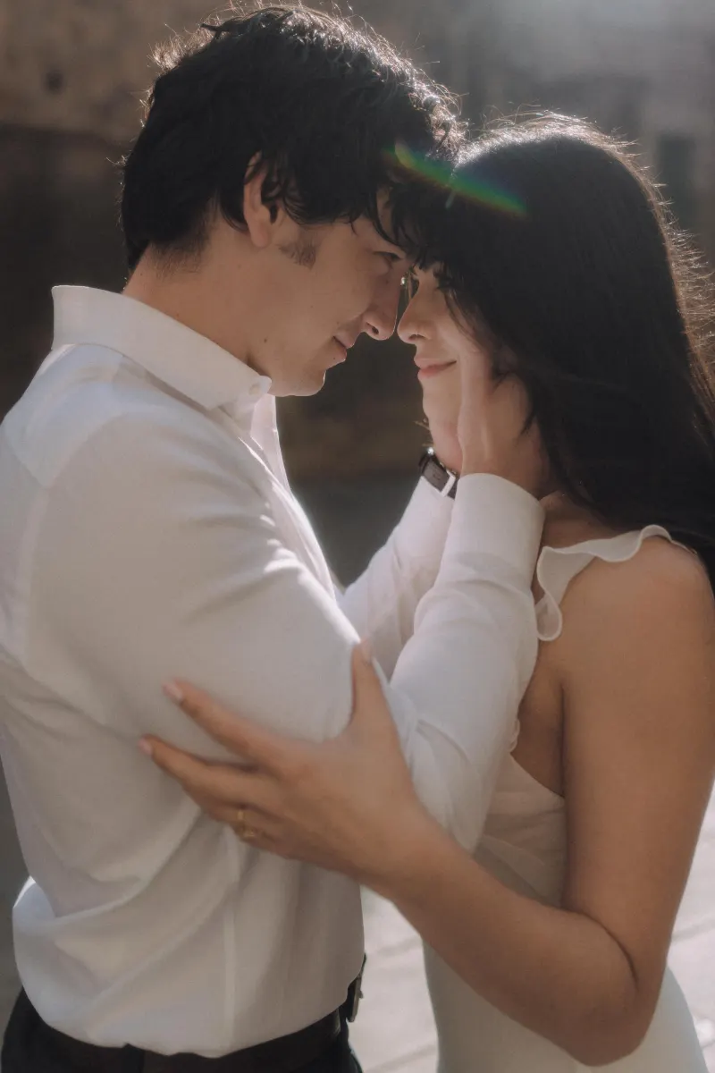 Couple shares an intimate, sunlit embrace, foreheads touching during a romantic couples & engagements photoshoot.