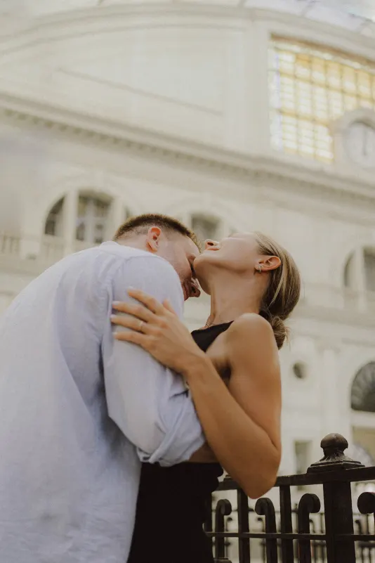 Couple sharing a joyful embrace by an ornate railing, captured during a couples & engagements photoshoot indoors.