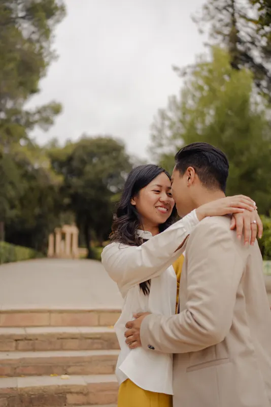 Couple sharing a joyful embrace on stone steps in a park, captured during a couples & engagements photoshoot.