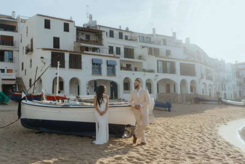 Couple sharing a joyful moment by a boat on a Mediterranean beach during a surprise proposal photoshoot.