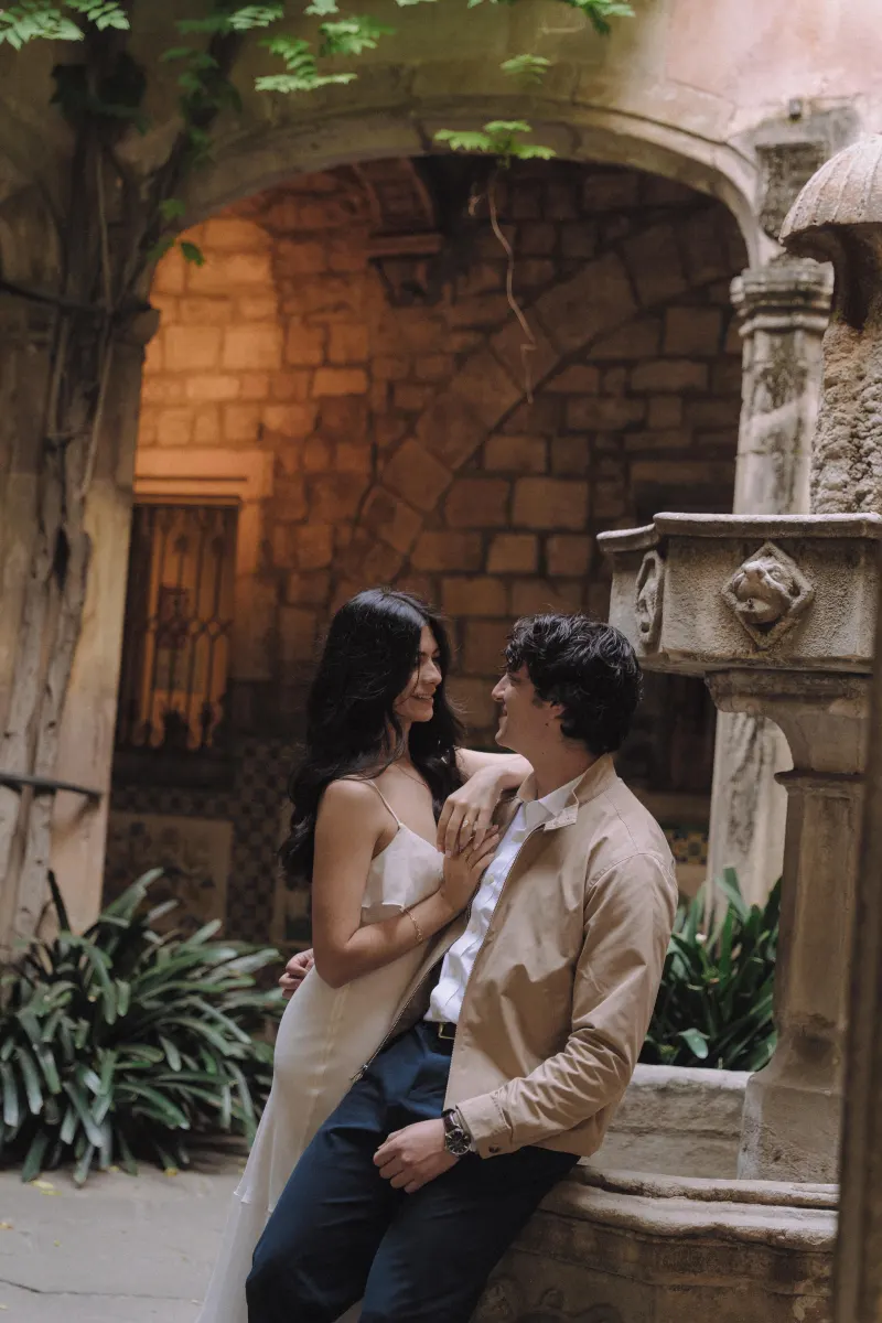 Couple sharing a loving gaze beside a stone fountain in a historic courtyard during a couples & engagements photoshoot.
