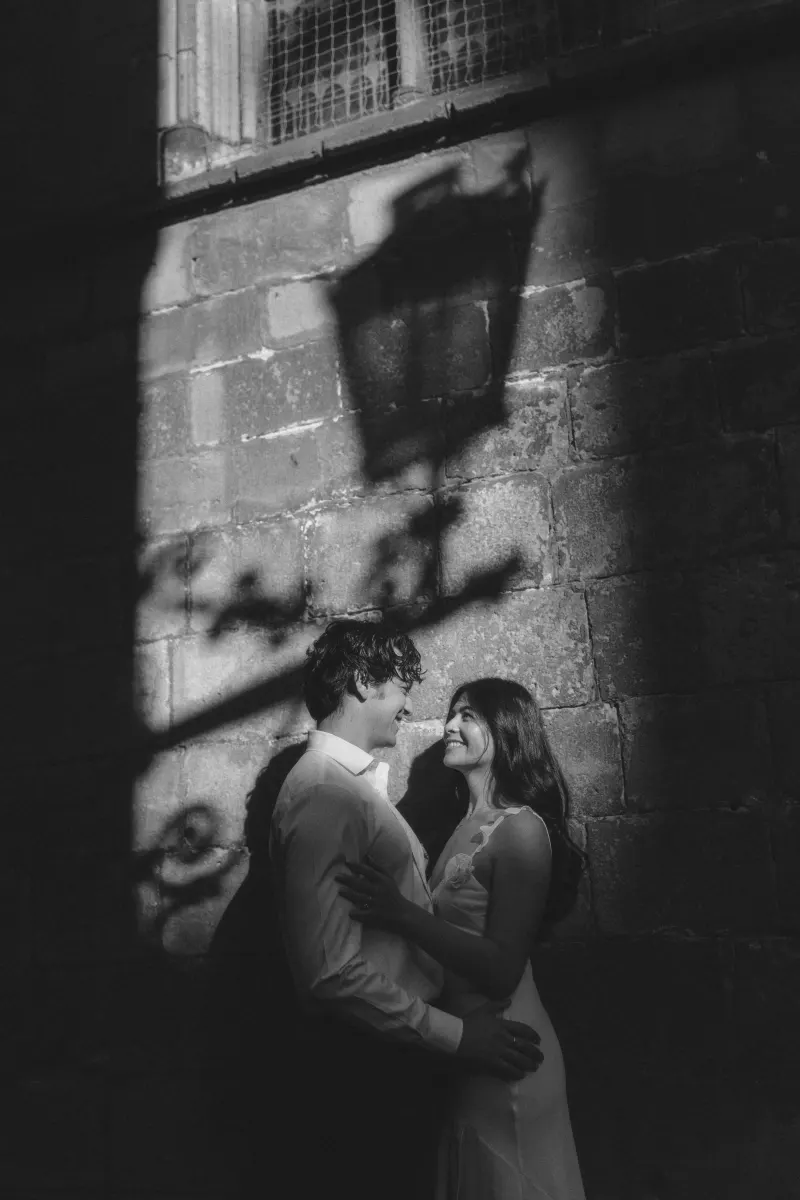 Couple sharing a loving gaze in dramatic sunlight against a historic stone wall during a couples & engagements photoshoot.
