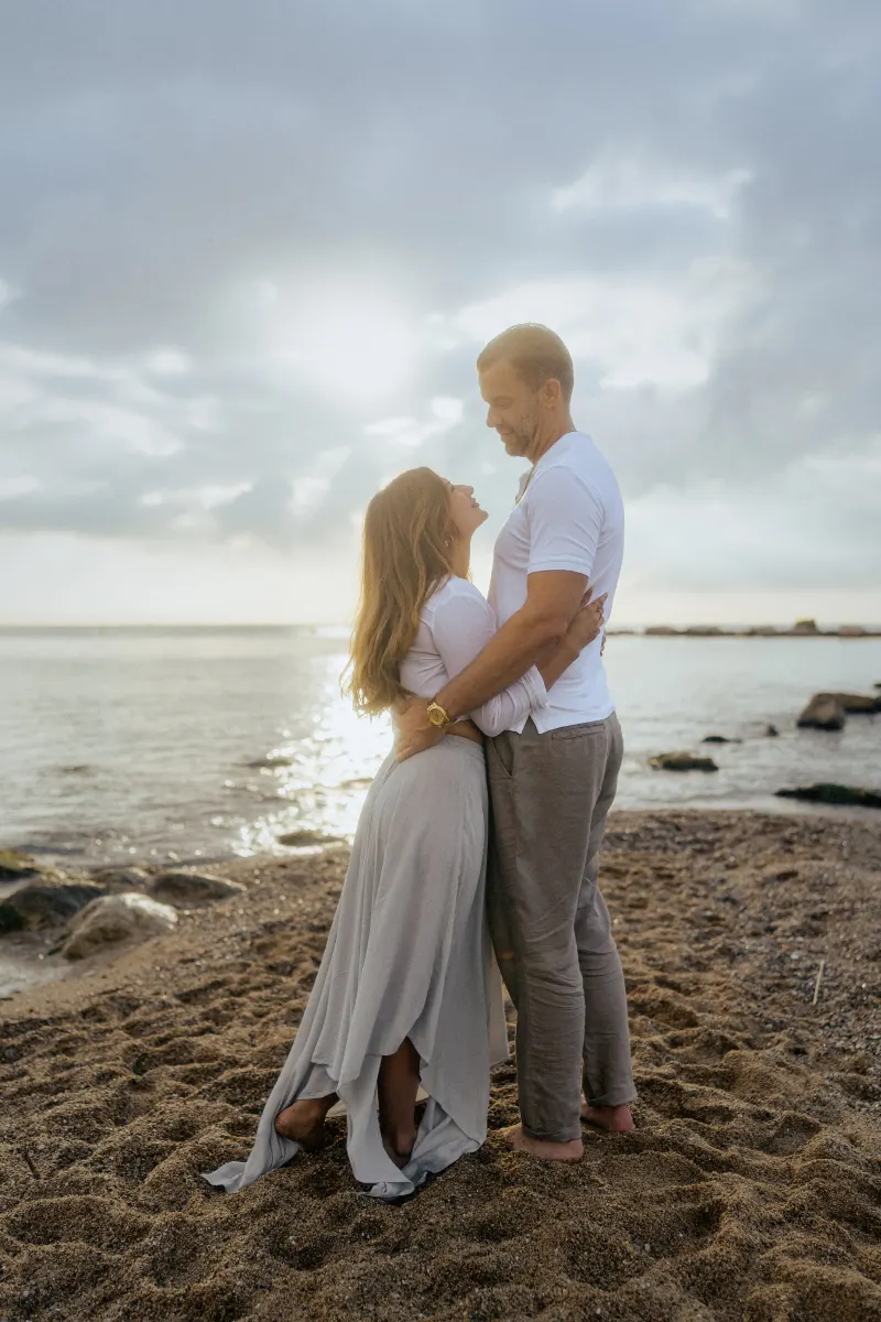 Couple sharing a loving gaze on a sandy beach at sunset, captured during a couples & engagements photoshoot.