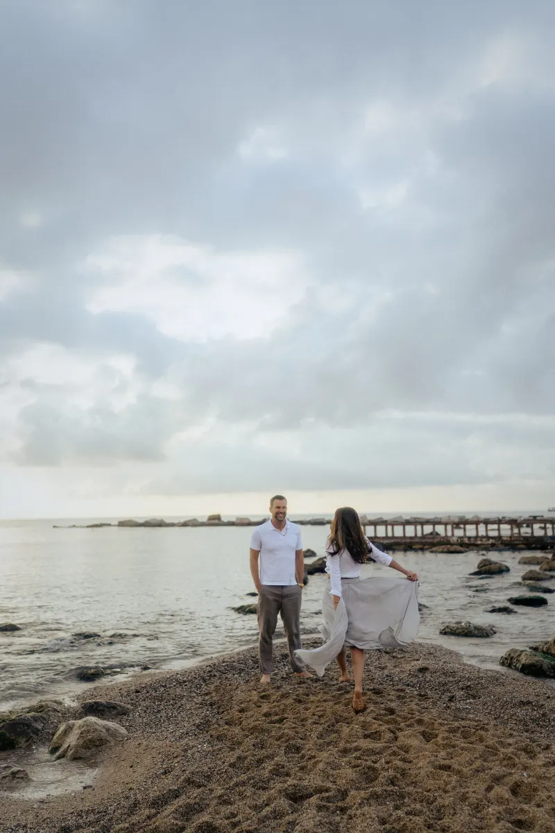 Couple sharing a playful moment on a rocky beach at sunset, captured during an engagement photoshoot session.