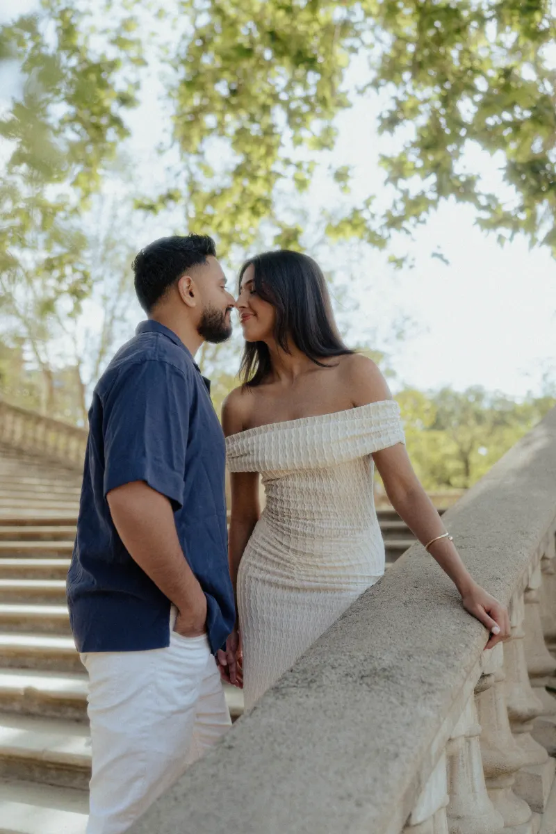 Couple sharing a playful, romantic moment on sunlit stone steps during an outdoor engagement photoshoot.