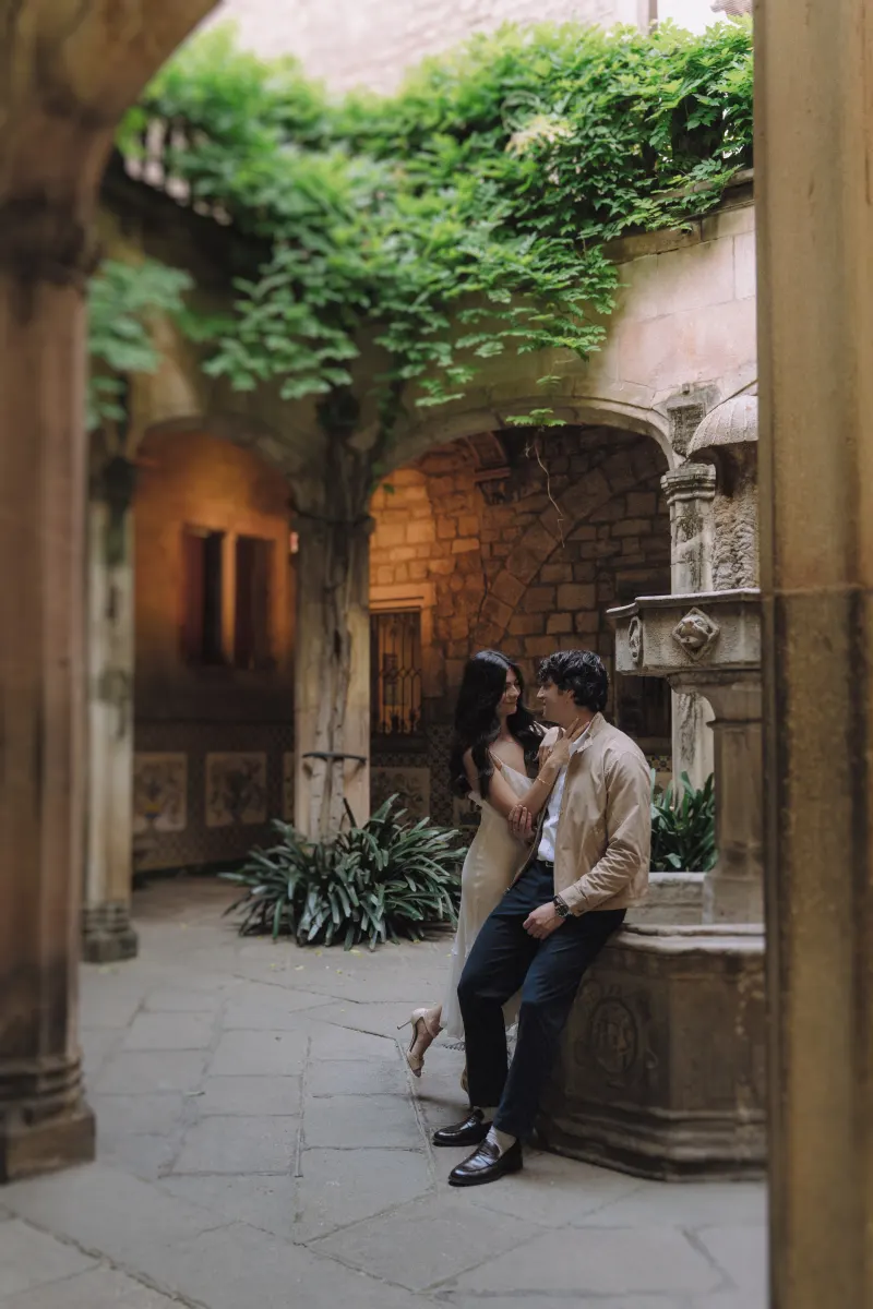 Couple sharing a quiet, affectionate moment by a stone fountain in a historic courtyard during an engagement photoshoot.