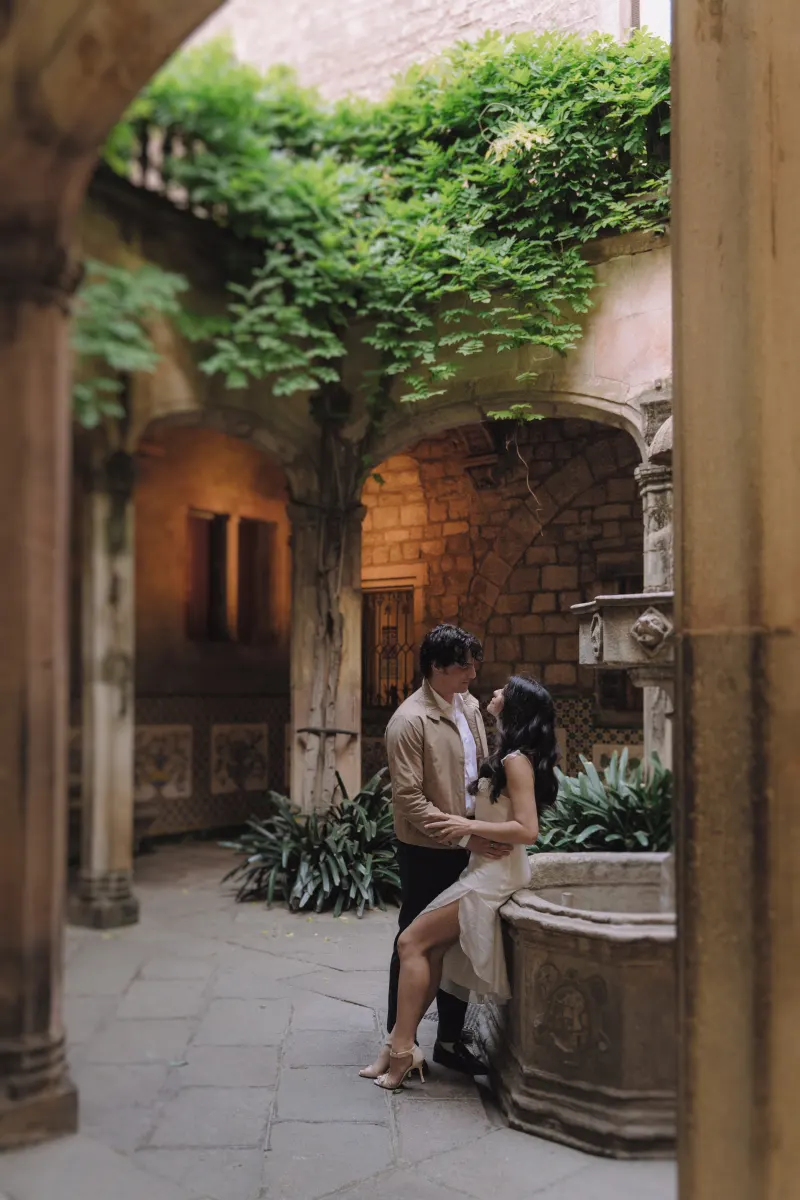Couple sharing a quiet embrace by a stone fountain in a romantic courtyard during an engagement photoshoot.