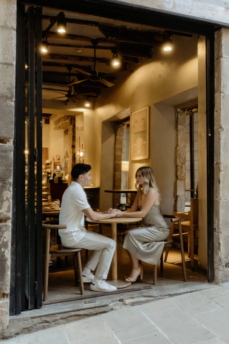 Couple sharing a quiet, intimate moment at a cozy Barcelona café during their Vacation Portraits photoshoot.