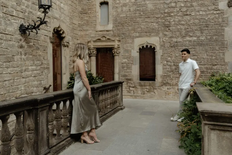 Couple sharing a quiet moment across a stone courtyard in Barcelona during their Vacation Portraits photoshoot.
