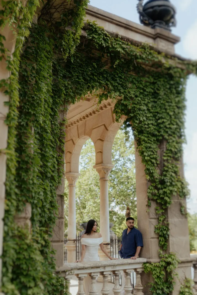 Couple sharing a quiet moment on a vine-covered stone balcony during a romantic engagement photoshoot in Barcelona.