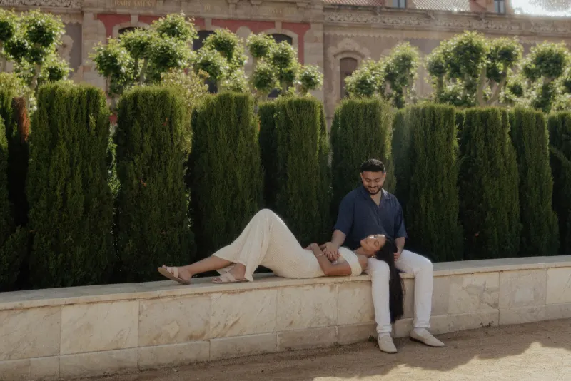 Couple sharing a relaxed, affectionate moment on a stone bench in a sunlit garden during an engagement photoshoot in Barcelon