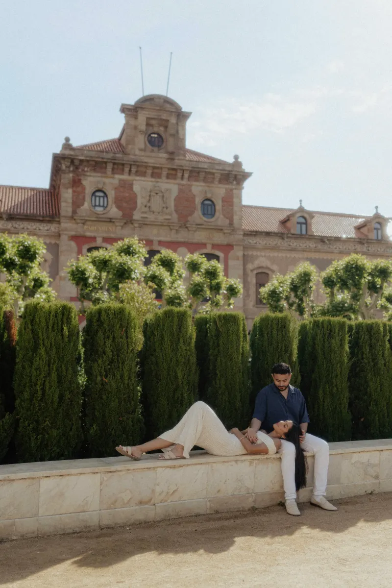Couple sharing a relaxed, affectionate moment on a sunlit stone bench during an engagement photoshoot in Barcelona.