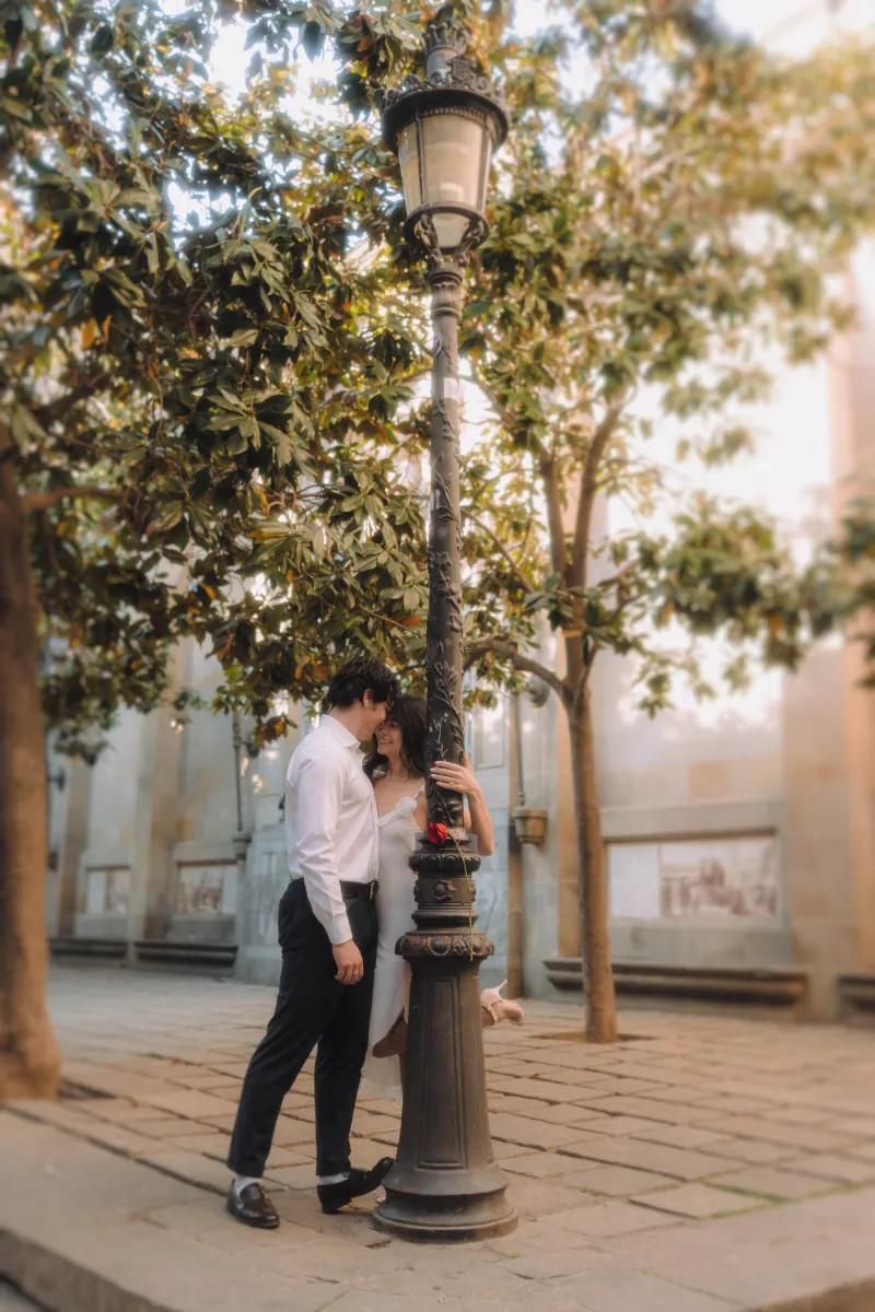 Couple sharing a romantic moment by a vintage lamppost in a sunlit courtyard during an engagement photoshoot.