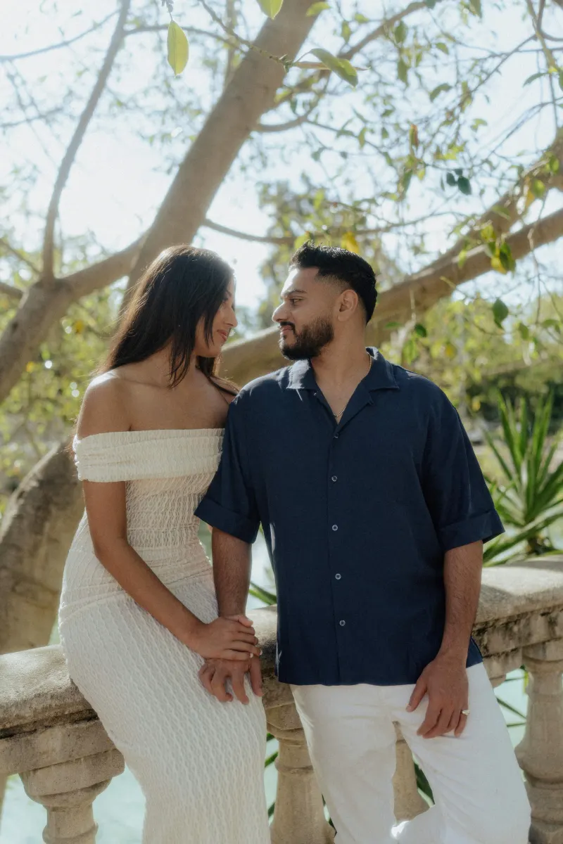 Couple sharing a soft, loving gaze while holding hands on a sunlit stone balcony during an engagement photoshoot.
