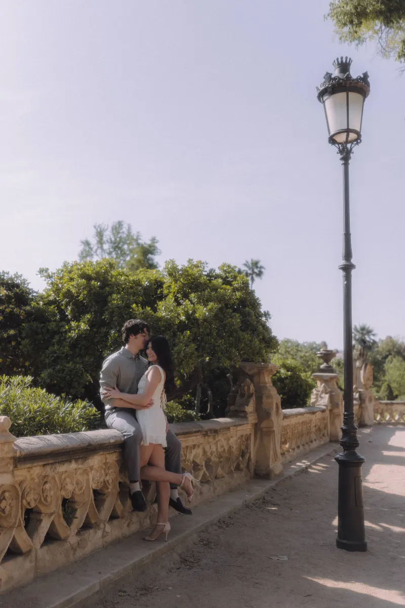Couple sharing a sweet embrace on a sunlit stone terrace during a couples & engagements photoshoot in a garden setting.