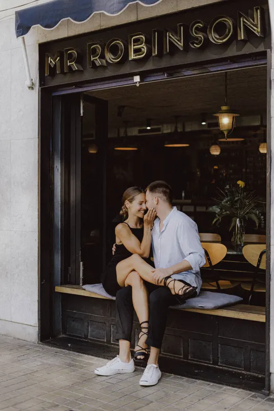 Couple sharing a sweet, intimate moment on a café bench during a couples & engagements photoshoot session.