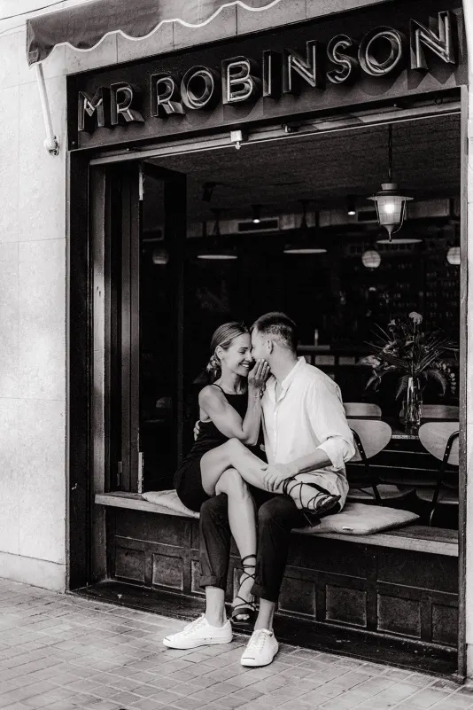 Couple sharing a sweet, intimate moment on a café windowsill during a couples & engagements photoshoot.