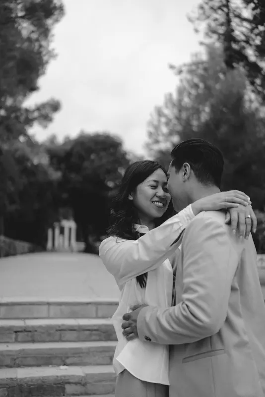 Couple sharing a tender embrace and smiling on stone steps during a couples & engagements photoshoot in the park.