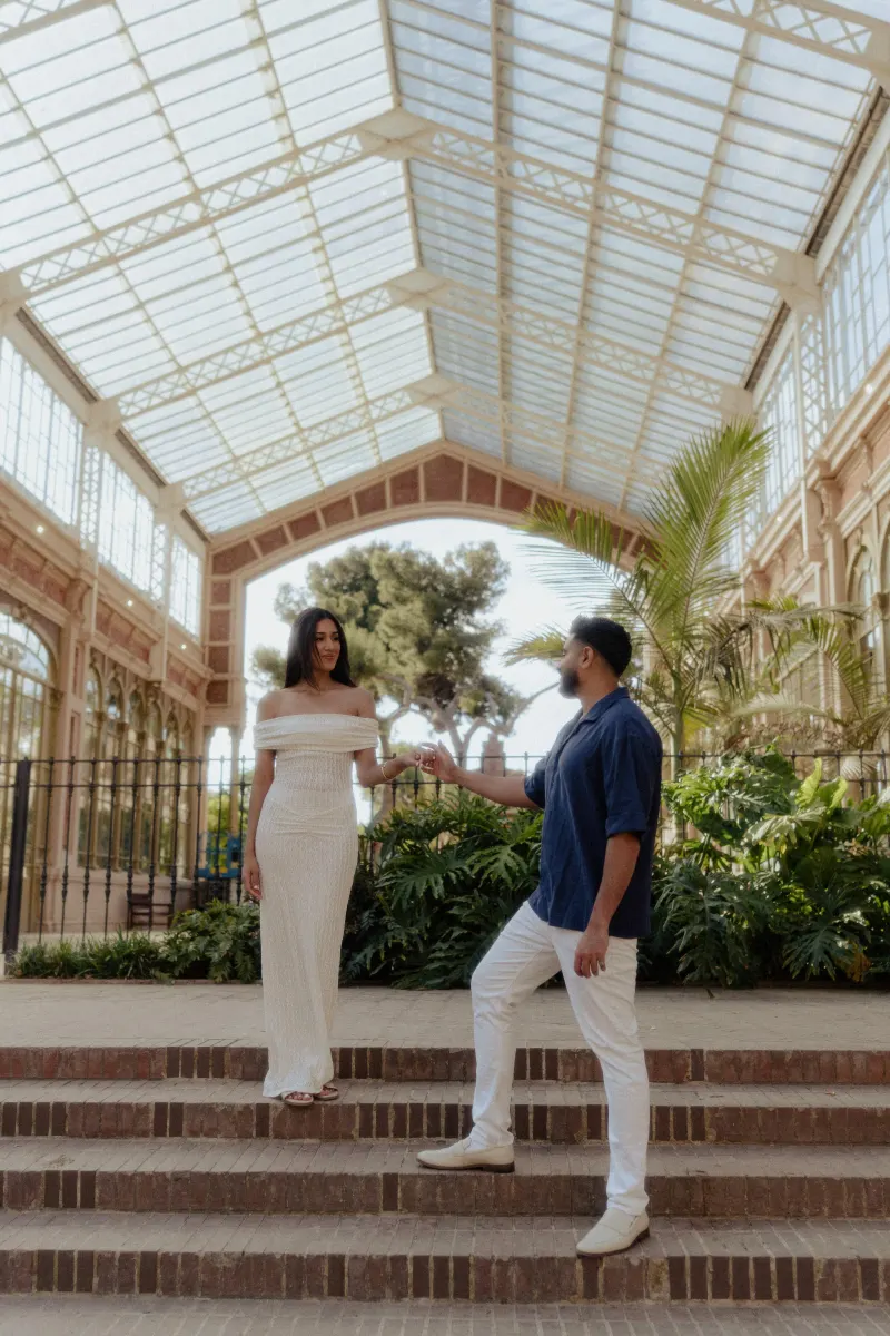 Couple sharing a tender moment on garden steps during an engagement photoshoot in a sunlit glass conservatory.