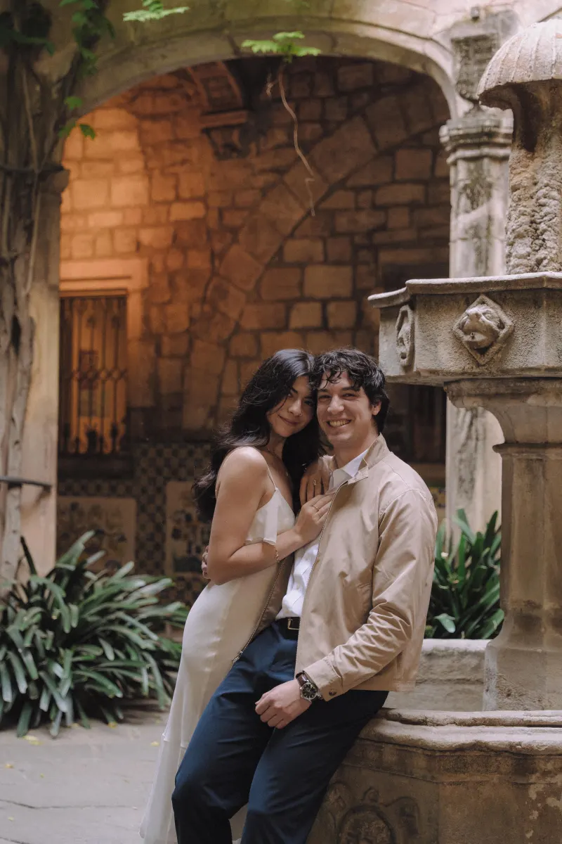 Couple sharing a warm embrace by a stone fountain in a historic courtyard during a couples & engagements photoshoot.