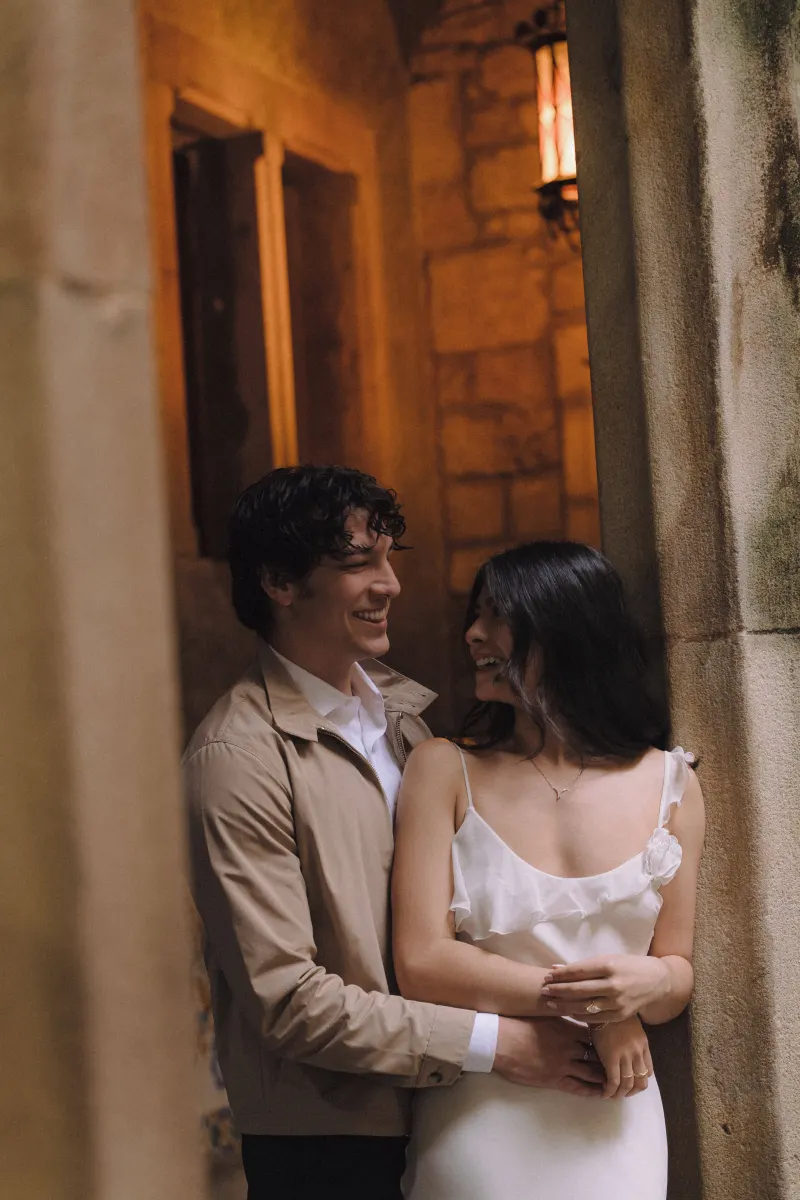 Couple sharing a warm smile and gentle embrace in a romantic stone archway during a couples & engagements photoshoot.