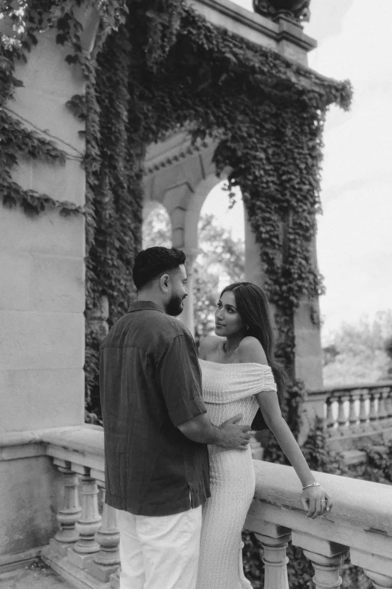 Couple sharing an intimate gaze on a vine-covered stone balcony during a romantic couples & engagements photoshoot.