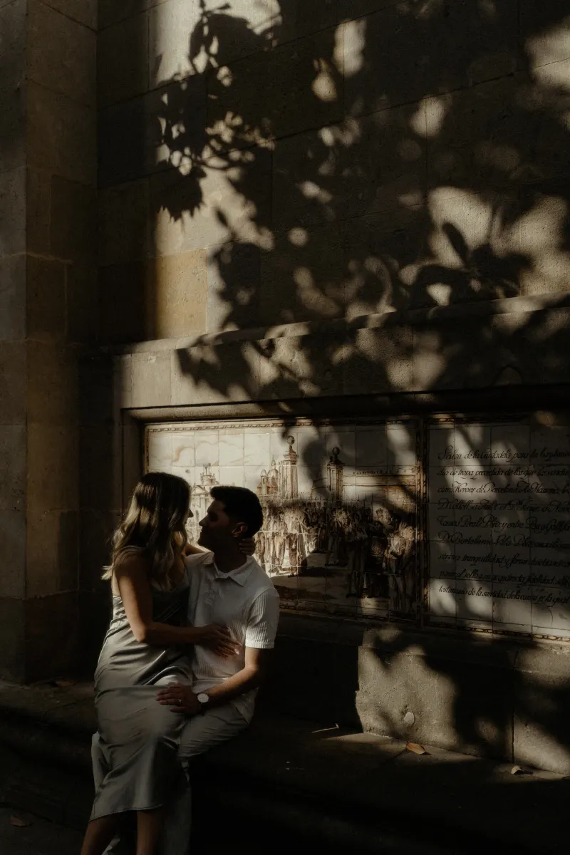 Couple sharing an intimate moment on a sun-dappled bench in Barcelona during a Vacation Portraits photoshoot.