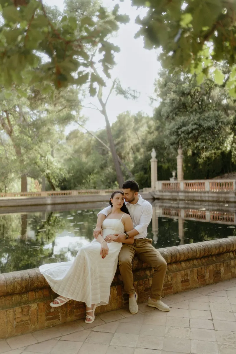 Couple sits by a peaceful garden pond, sharing a quiet embrace during a couples & engagements photoshoot.