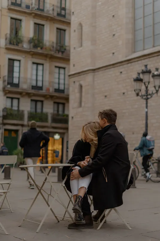 Couple sits close at a café table in Barcelona’s old town, sharing a quiet moment during an engagement photoshoot
