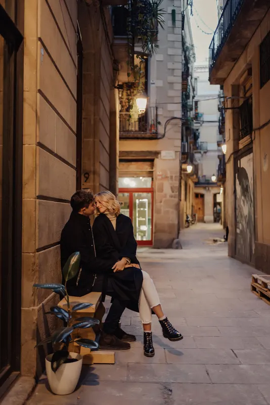 Couple sits close on a bench in a cozy Barcelona alley, sharing a loving moment during a couples & engagements photoshoot.