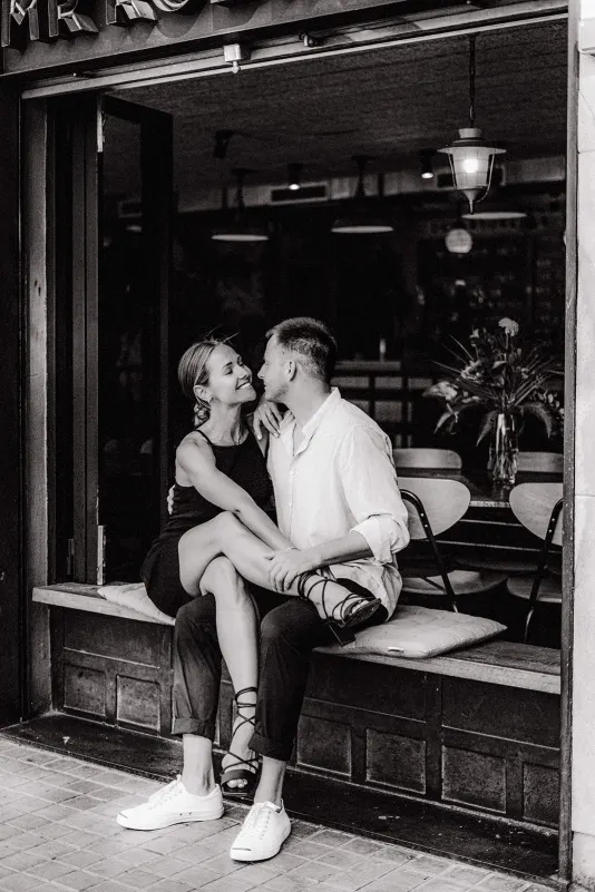 Couple sits close on a café bench, sharing a loving smile during a couples & engagements photoshoot session.