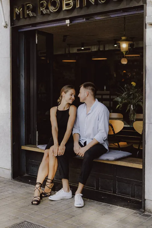 Couple sits close on a café bench, sharing a quiet, affectionate moment during a couples & engagements photoshoot.