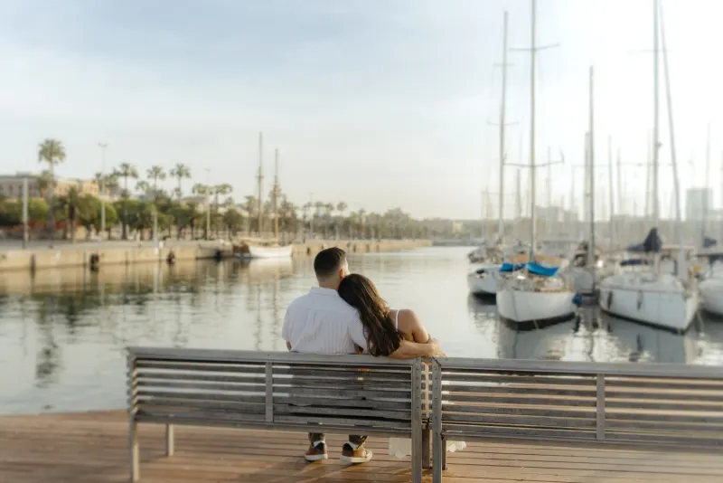 Couple sits close on a marina bench, sharing a quiet moment during an engagement photoshoot by the water.