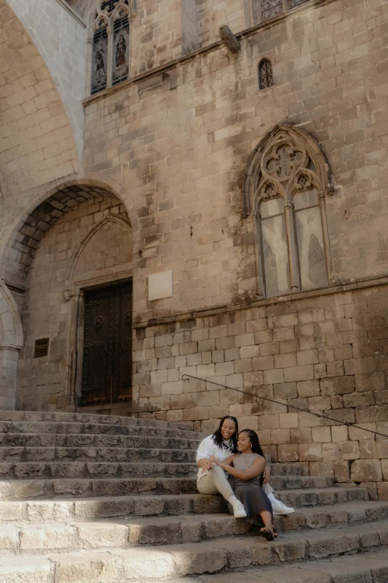 Couple sits close on ancient stone steps in Barcelona, sharing a joyful moment during their surprise proposal photoshoot.