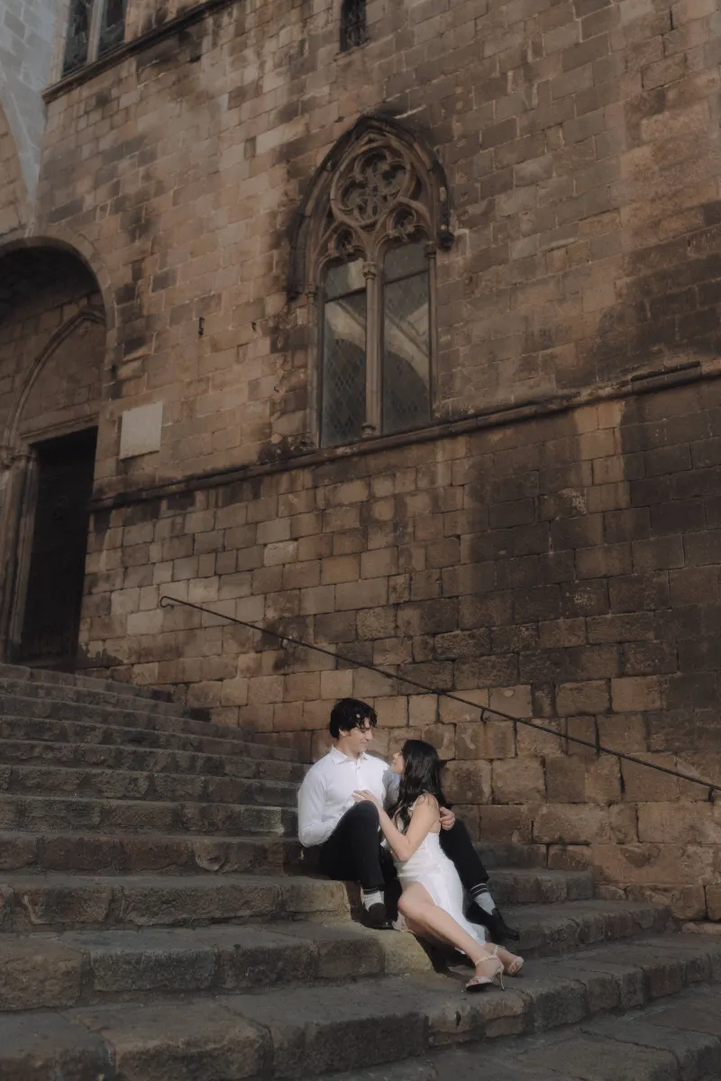 Couple sits close on historic stone steps, sharing a loving gaze during a couples & engagements photoshoot in Barcelona.