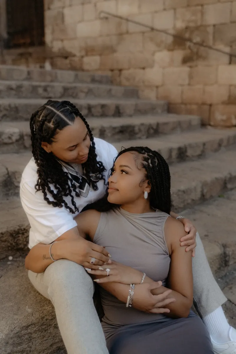 Couple sits close on stone steps in Barcelona, sharing a loving gaze during their surprise proposal photoshoot.