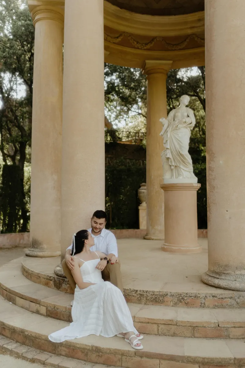 Couple sits close on stone steps of a classical pavilion, sharing a tender moment during an engagement photoshoot.