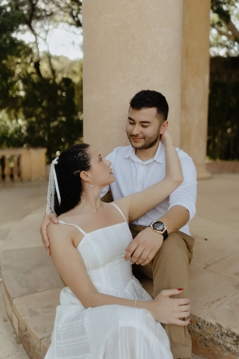 Couple sits close on stone steps, sharing a loving gaze during a couples & engagements photoshoot at a garden pavilion.