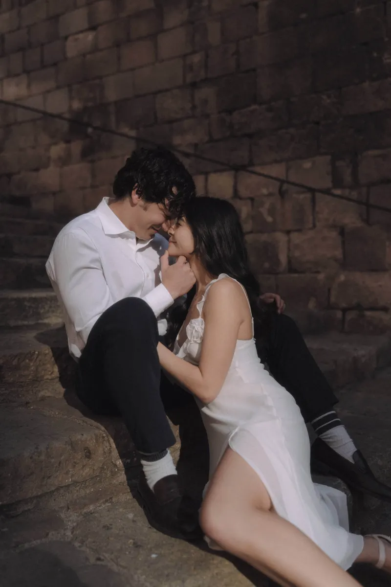 Couple sits close on sunlit stone steps, sharing an intimate moment during a couples & engagements photoshoot.