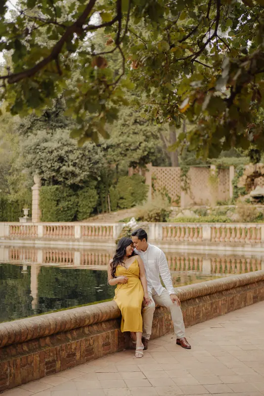 Couple sits close together by a peaceful pond, sharing a loving moment during their couples & engagements photoshoot.