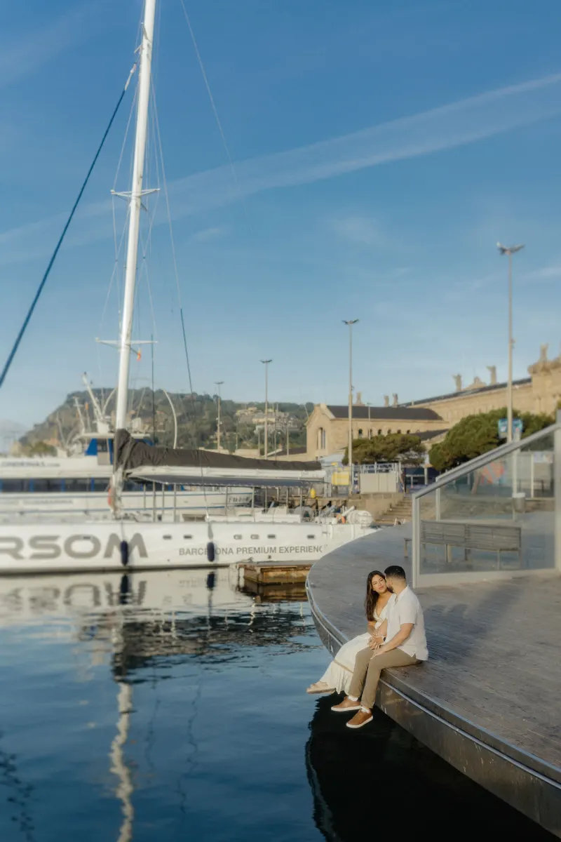 Couple sits together at a marina’s edge, sharing a quiet, intimate moment during their engagement photoshoot.
