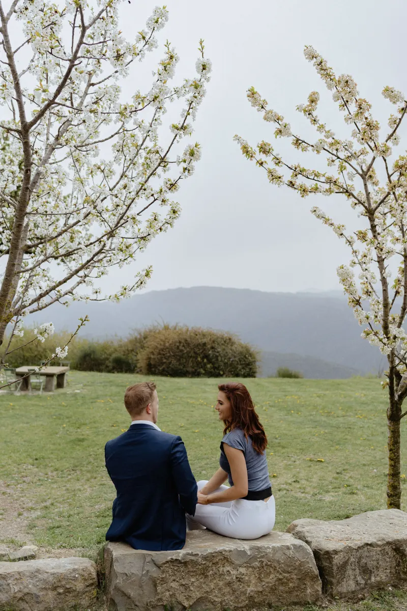 Couple sits together on a stone ledge, sharing a quiet, joyful moment before their countryside surprise proposal session.