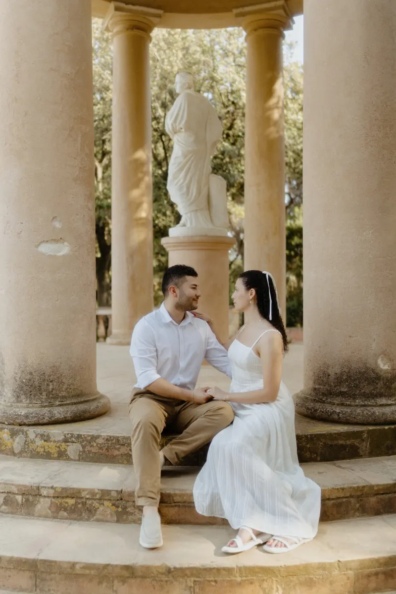 Couple sits together on stone steps between columns, sharing a gentle gaze during a couples & engagements photoshoot.