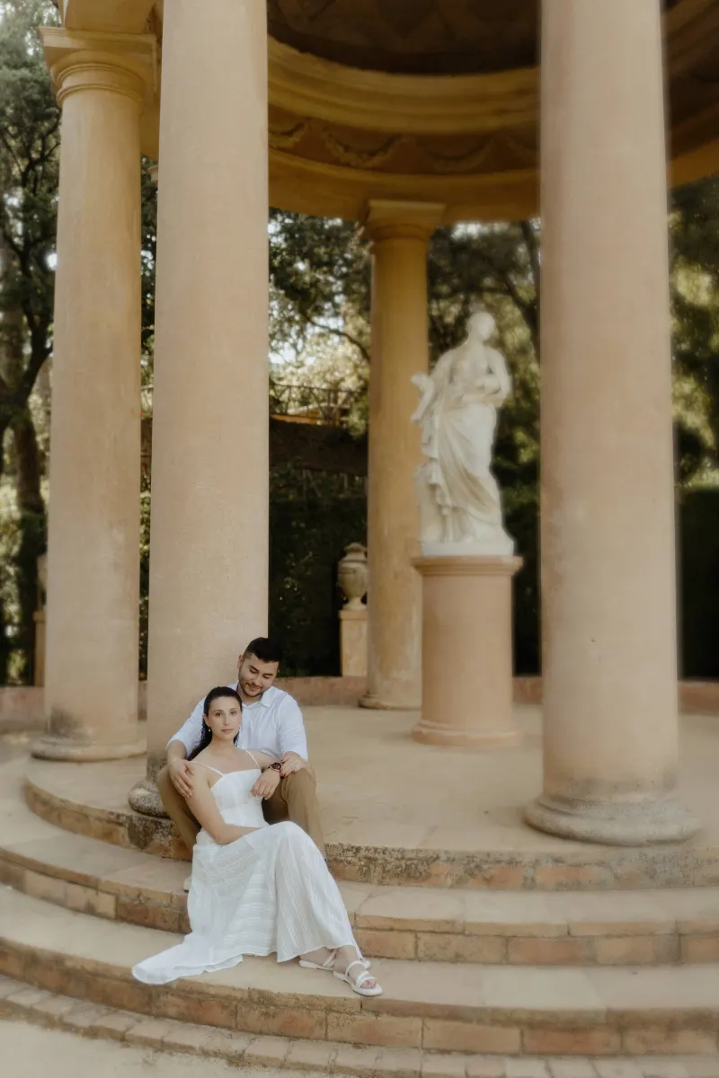 Couple sits together on stone steps of a classical pavilion, sharing a peaceful moment during an engagement session.