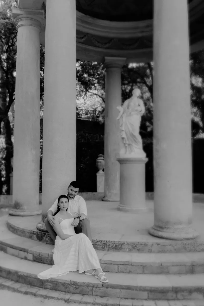 Couple sits together on stone steps of a classical pavilion, sharing a quiet embrace during an engagement session.