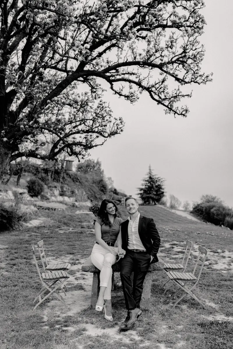 Couple sits together under a blooming tree, sharing a happy moment before their countryside surprise proposal photoshoot.