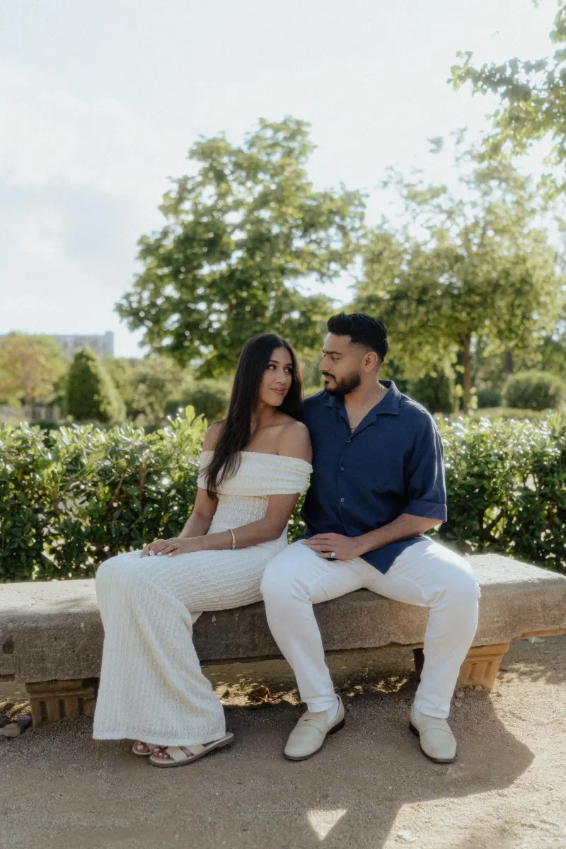 Couple sitting close on a stone bench, sharing a quiet, affectionate gaze during a couples & engagements photoshoot outdoors.