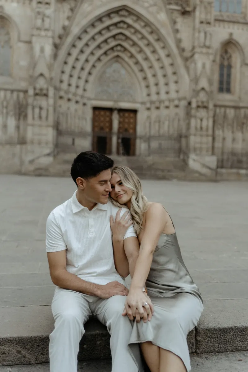 Couple sitting close on cathedral steps in Barcelona, sharing a tender moment during a Vacation Portraits photoshoot.