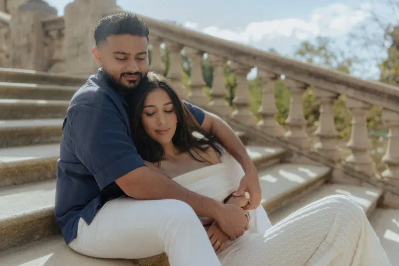 Couple sitting close on sunlit stone steps, sharing a peaceful embrace during a couples & engagements photoshoot.
