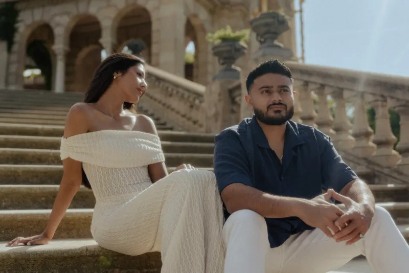 Couple sitting together on sunlit stone steps, sharing a quiet, thoughtful moment during an engagement photoshoot.